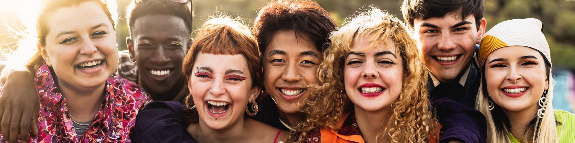 A group of friends smiling and proudly holding up the rainbow-coloured PRIDE flag