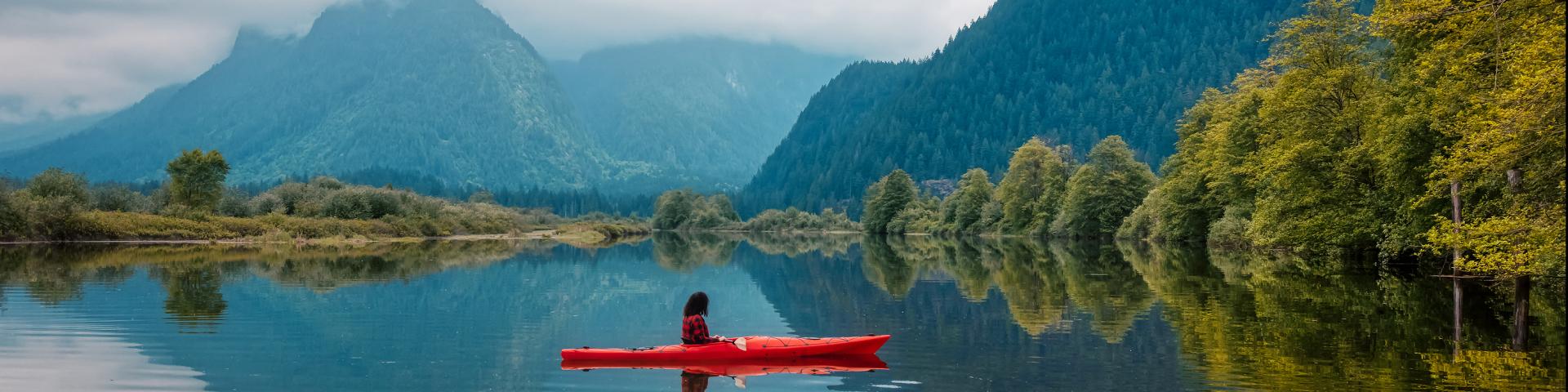 Photo of kayaker surrounded by water and beautiful mountains and trees during a fall day in Vancouver.