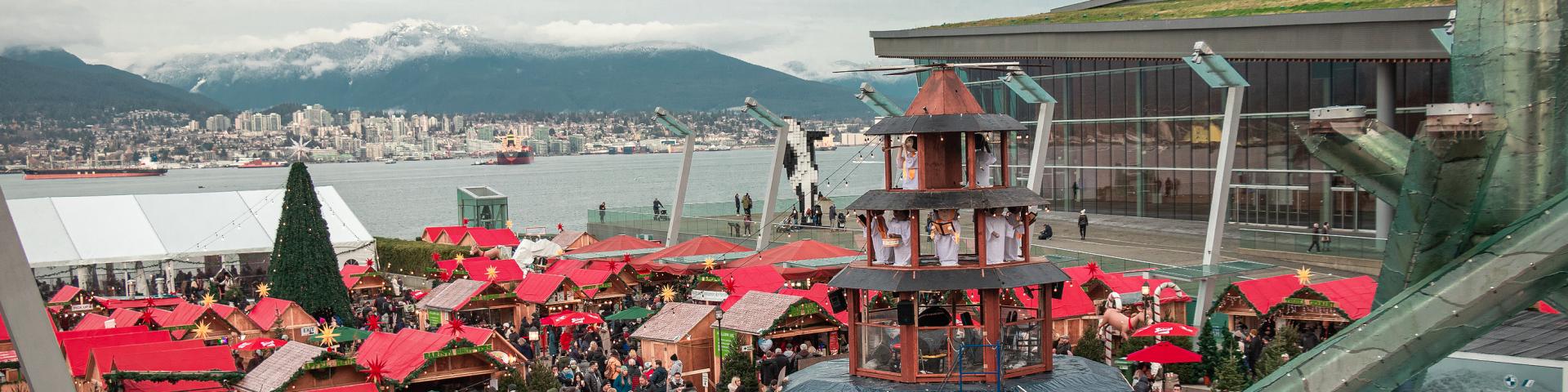 Photo of booths at the Vancouver Christmas Market overlooking the skyline of mountains at Jack Poole Plaza in Coal Harbour