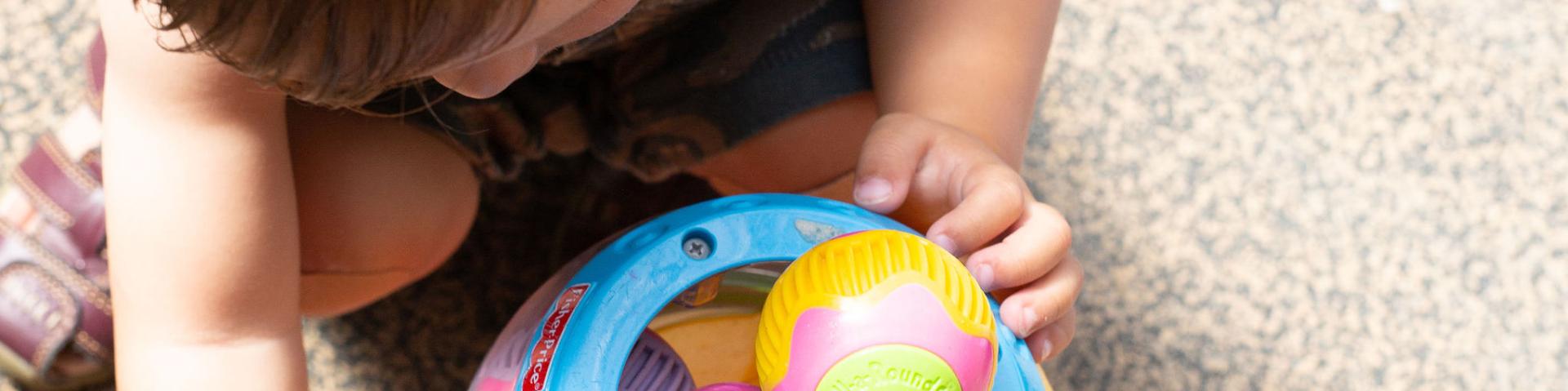 Kid playing with a colourful toy bucket with balls inside