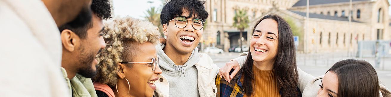 A picture of a group of diverse young people smiling at each other in front of a building.