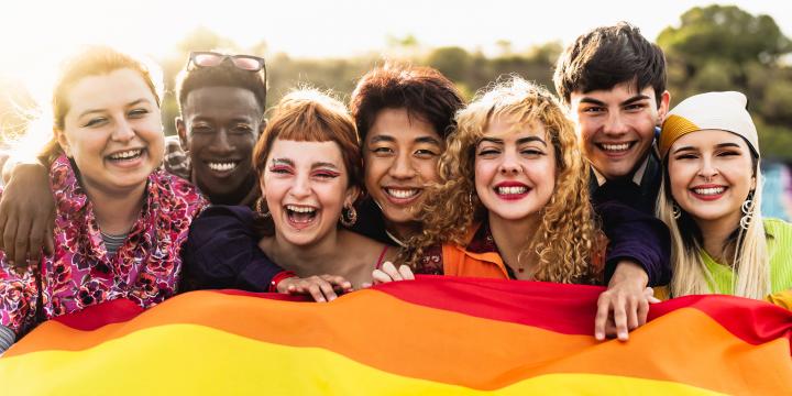 A group of friends smiling and proudly holding up the rainbow-coloured PRIDE flag