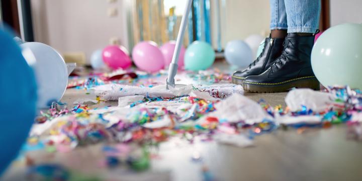 Person with pushbroom cleaning mess of floor in room after party confetti, morning after party celebration