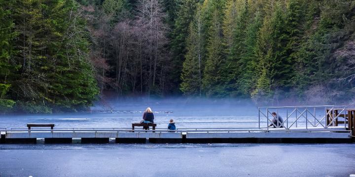 A family sitting in front of a misty lake in Lynn Canyon Park