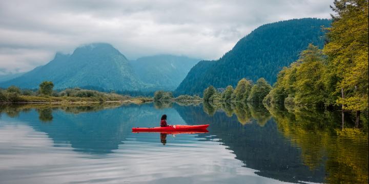 Photo of kayaker surrounded by water and beautiful mountains and trees during a fall day in Vancouver.