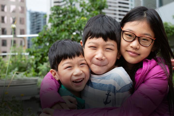Three kids smiling and hugging each other.