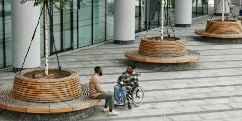 Two people who are Black-presenting, sitting across from each other, with one person in a wheelchair