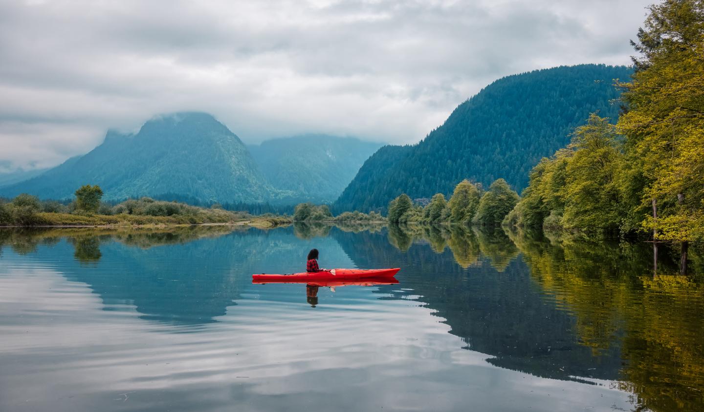 Photo of kayaker surrounded by water and beautiful mountains and trees during a fall day in Vancouver.