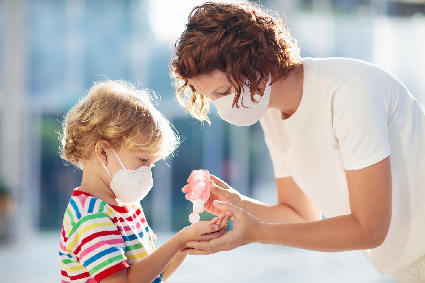 Mother and Child with hand sanitizers. Both wearing masks.