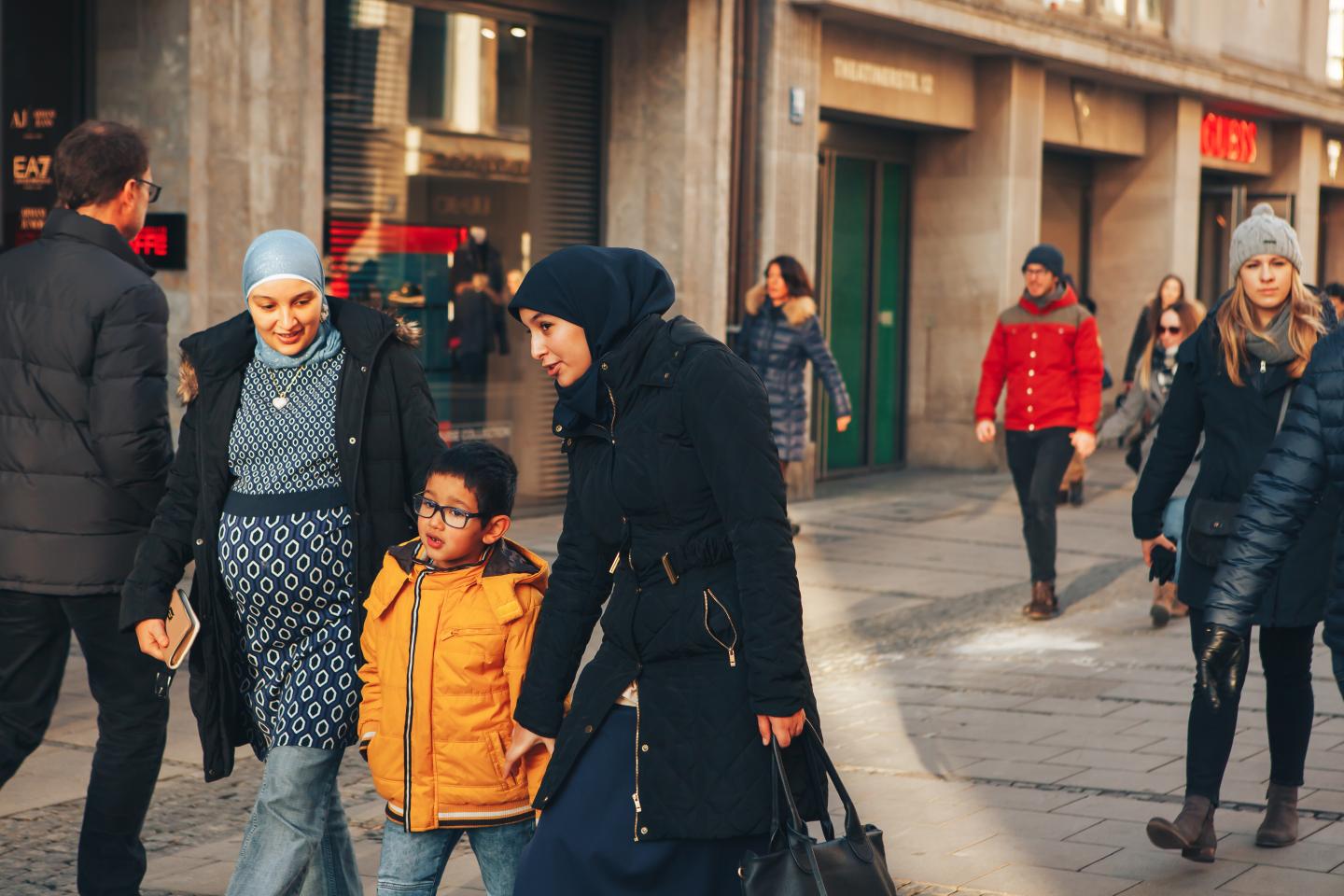Two adults in hijab with a child walking on a street with other people