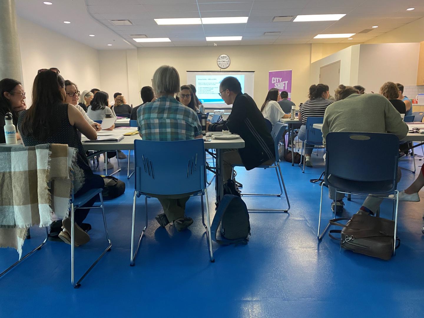 Room of people around tables in a workshop setting