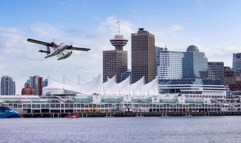 Skyline Vancouver along Coal Harbour, with Canada Place, the Vancouver lookout and Pan Pacific visible  along the water. A seaplane is also taking off.