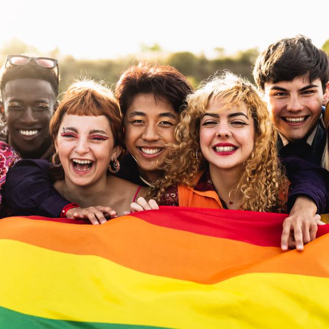 A group of friends smiling and proudly holding up the rainbow-coloured PRIDE flag