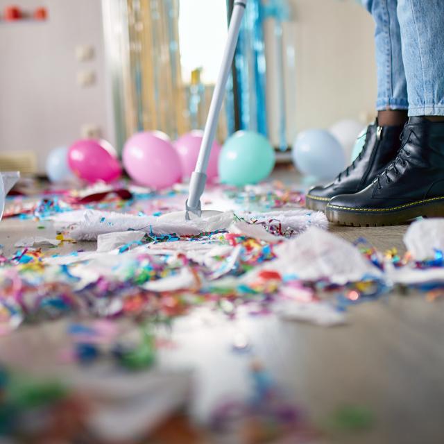 Person with pushbroom cleaning mess of floor in room after party confetti, morning after party celebration