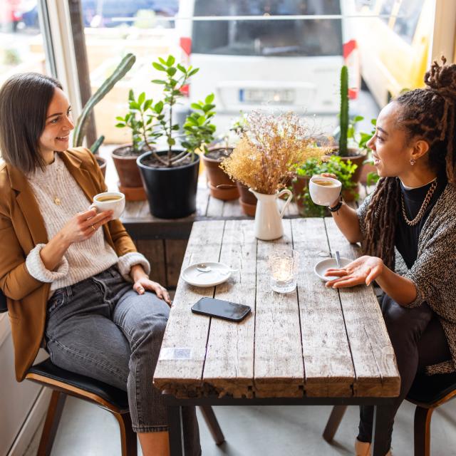 Two female business professionals having conversation over a cup of coffee at local cafe. Businesswomen talking while having coffee at a coffee shop.