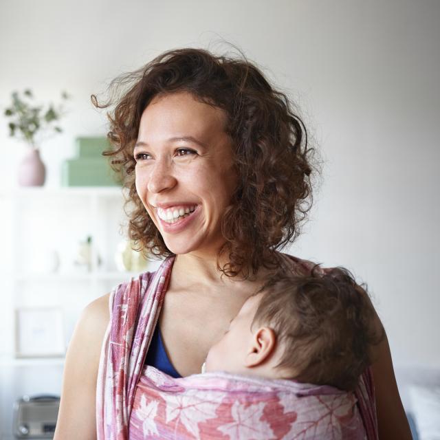 Smiling women carrying a sleeping baby on a sling 
