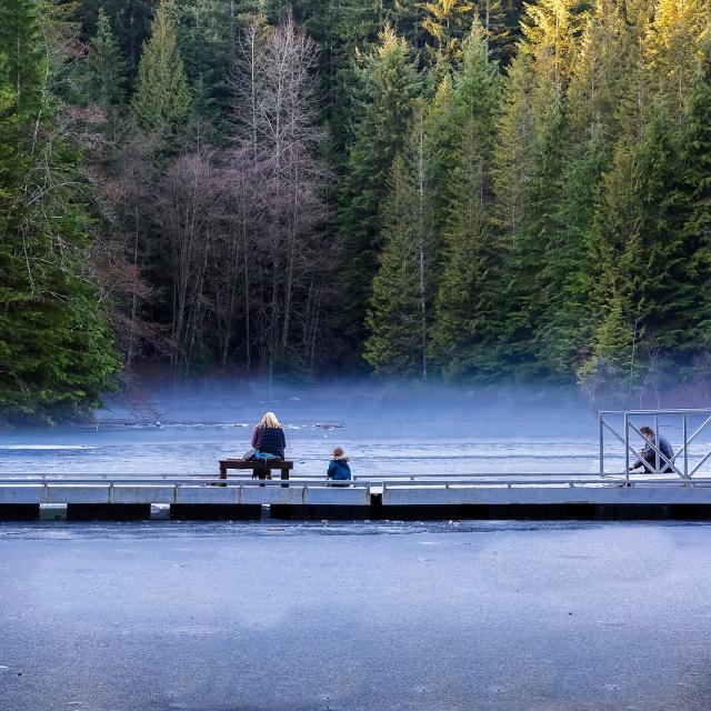 A family sitting in front of a misty lake in Lynn Canyon Park