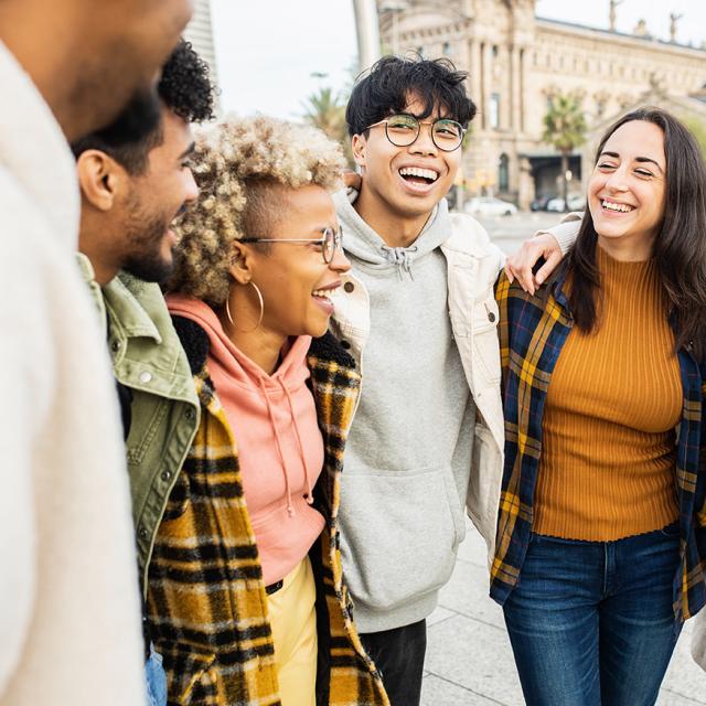 A picture of a group of diverse young people smiling at each other in front of a building.