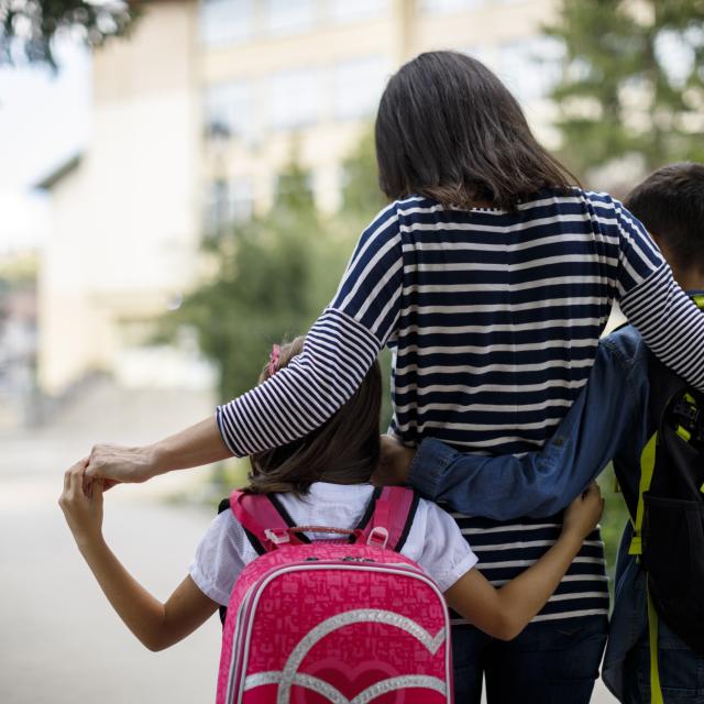Female walking kids with backpacks to school