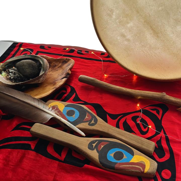  A drum, drumsticks, and feathers on a red blanket.